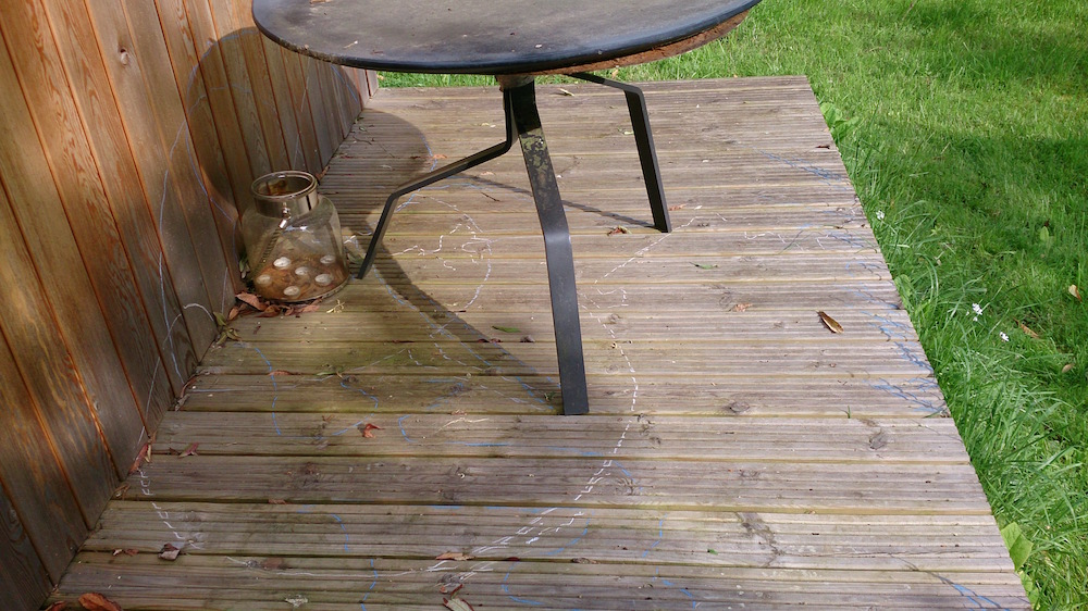 a round metal table and blue and white lines drawn around shadows on the decking