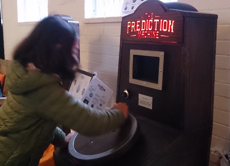 a girl turning the handle to power The Prediction Machine at Polka Theatre