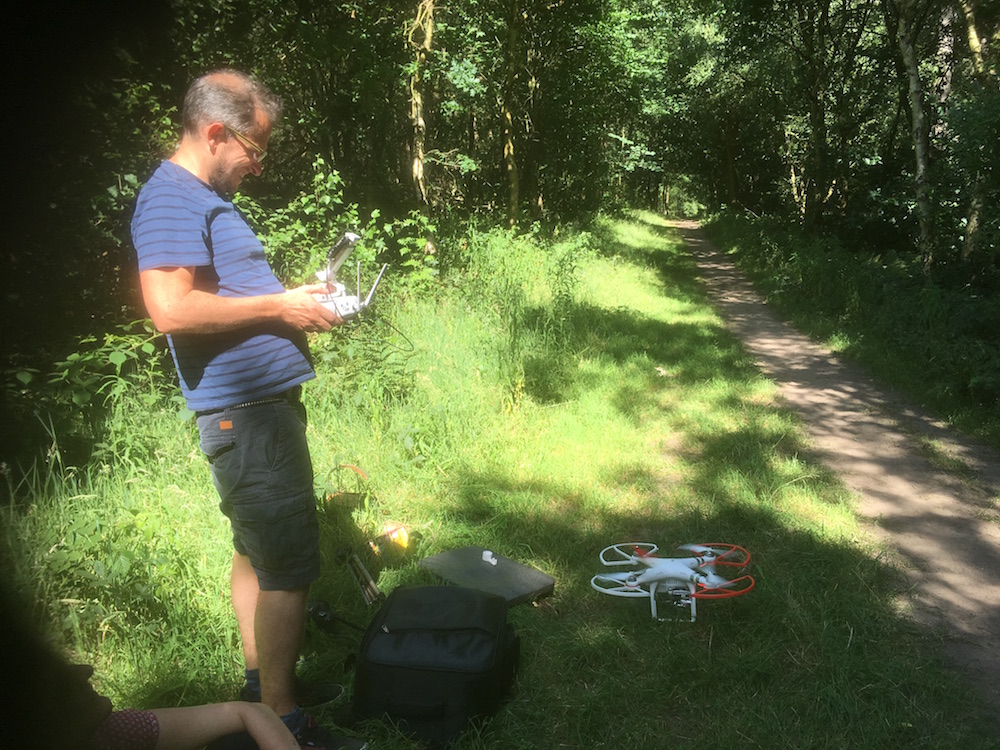 Matt and the drone on a path in the forest with sunlight behind him
